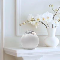 cremation small urns for ashes cremation memorial gifts A beautifully decorated white urn with a silver lid and accents is displayed on top of a minimalist shelf