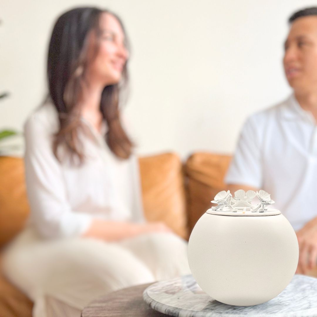 keepsake urns cat urn two people engaged in conversation, with a woman on the left and a man on the right, both slightly out of focus, while a decorative urn is prominently displayed in the foreground on a table