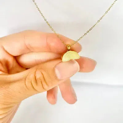 a hand holding a gold cremation necklace with a rainbow pendant