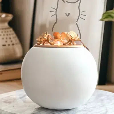 a white urn with a gold lid on top of a marble table with a picture of a cat against the wall